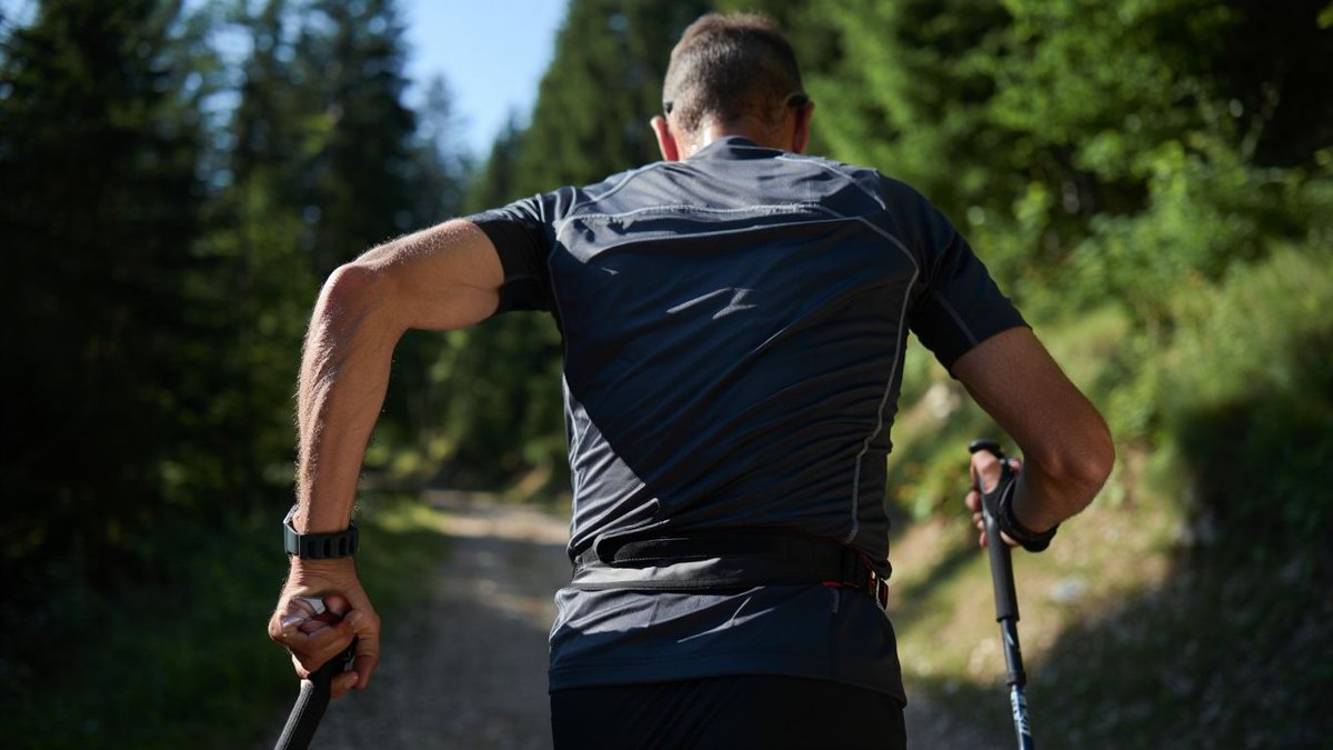 Traileur amateur vu de dos utilisant des bâtons sur un sentier de montagne sans marque visible