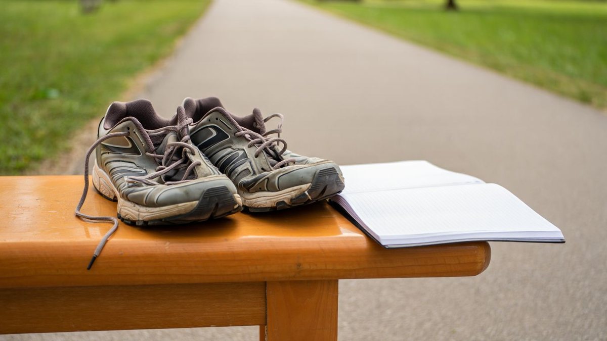 Paire de chaussures de running usées posée près d’une piste et d’un carnet d’entraînement