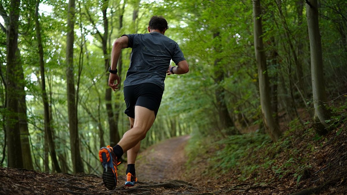 Coureur de trail amateur descendant un sentier forestier technique avec appuis courts sans marque visible