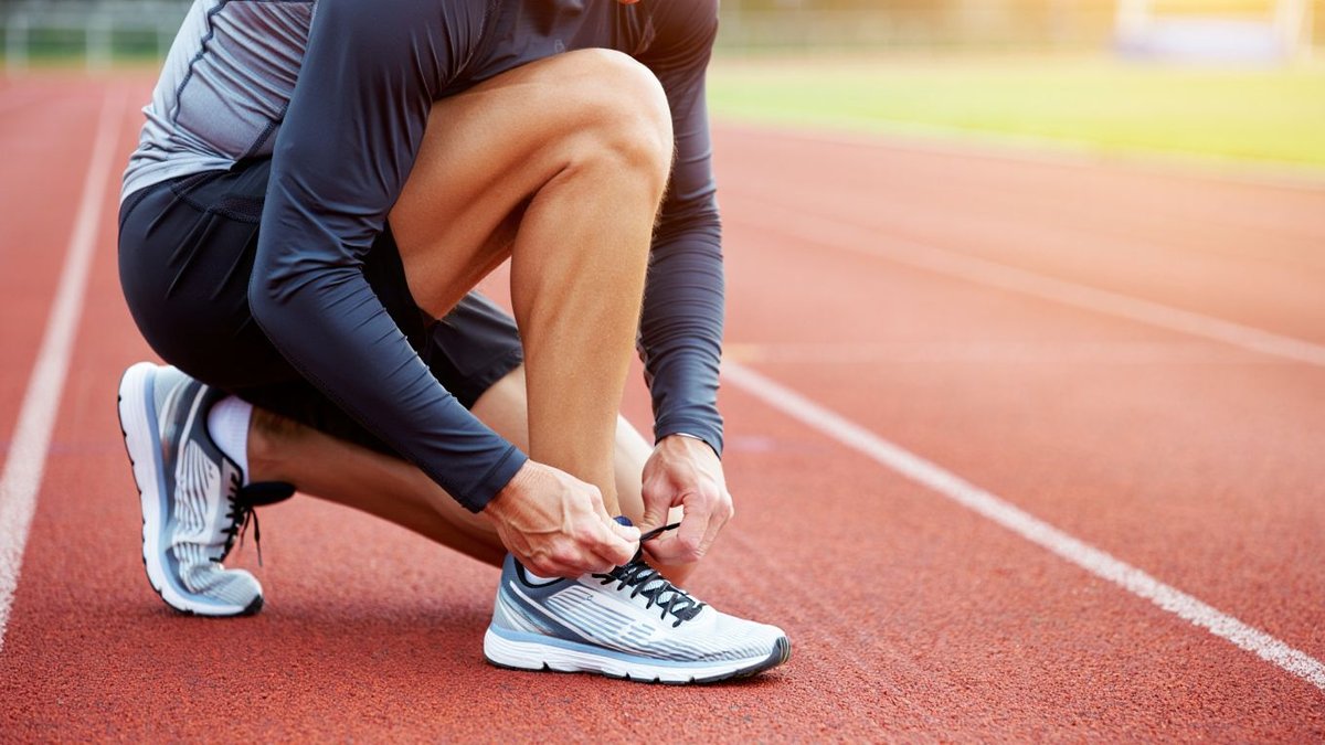 Coureur amateur attachant des chaussures de running neutres sur une piste extérieure sans logo ni texte visible