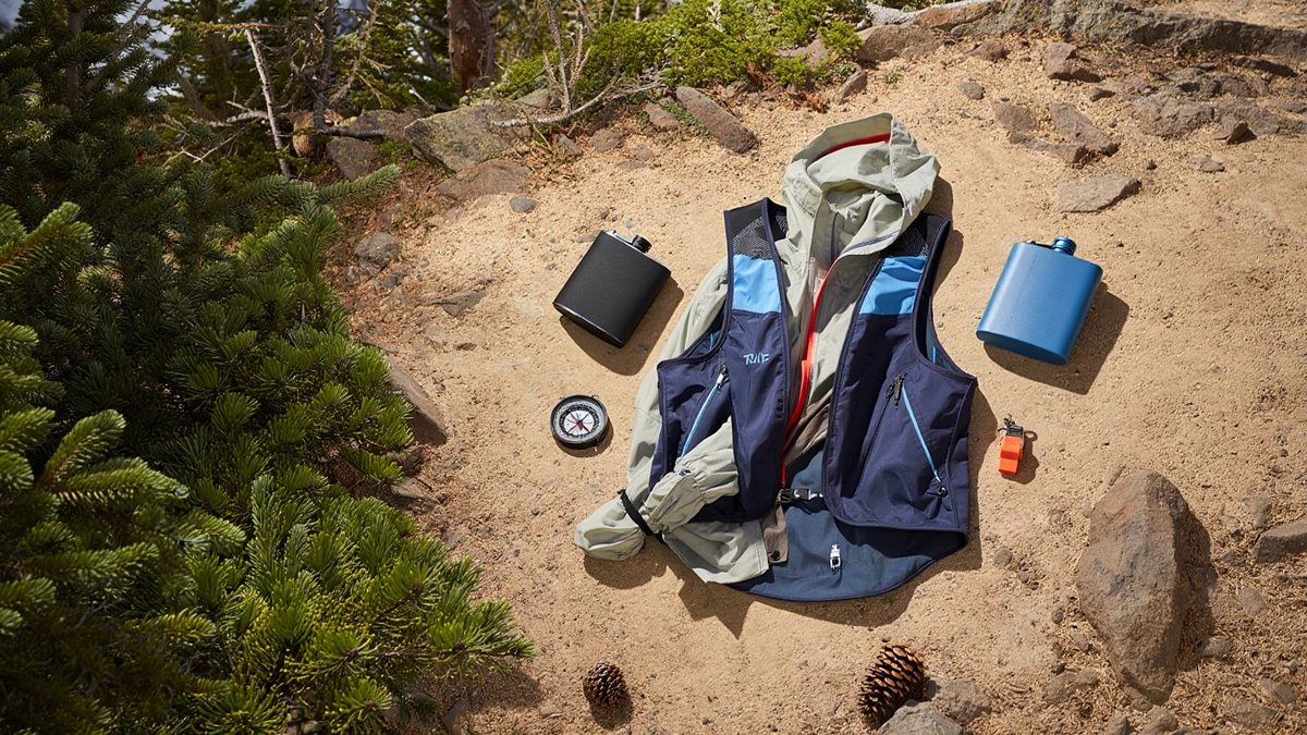 Sac de trail ouvert avec flasques et veste légère sur un sentier naturel sans marque ni texte visible