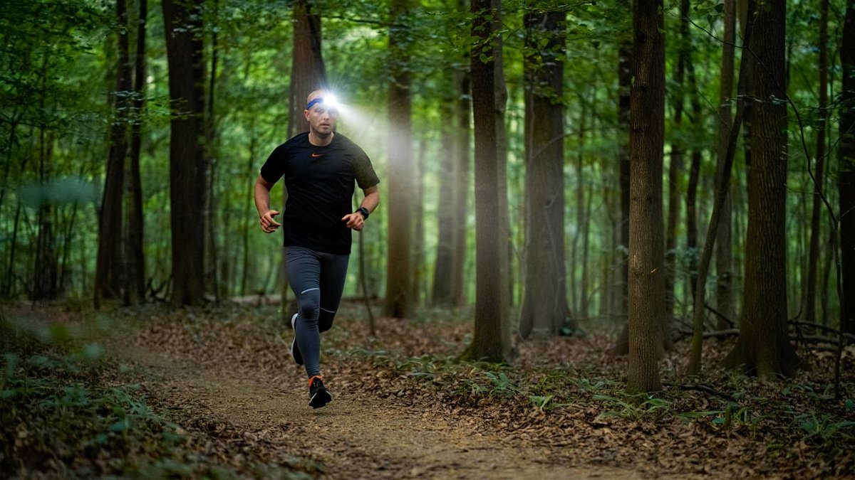 Traileur adulte courant au crépuscule avec lampe frontale allumée sur sentier forestier sans marque ni texte