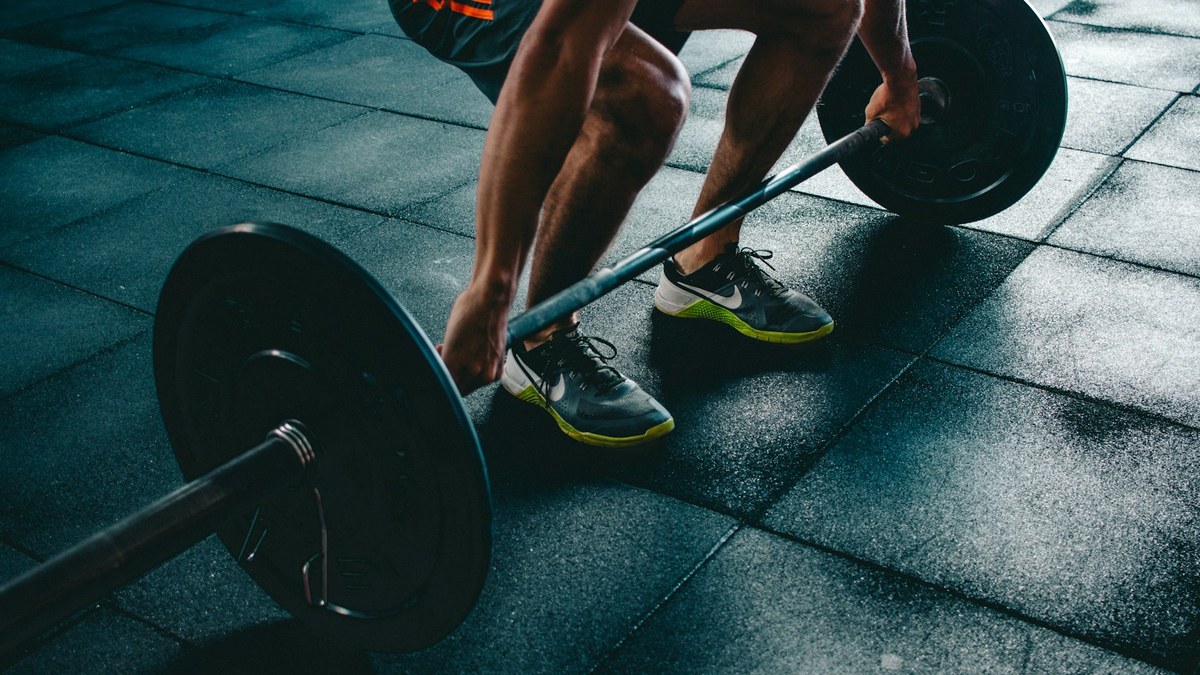 Sportive réalisant un soulevé de terre roumain avec haltères dans une salle de sport lumineuse