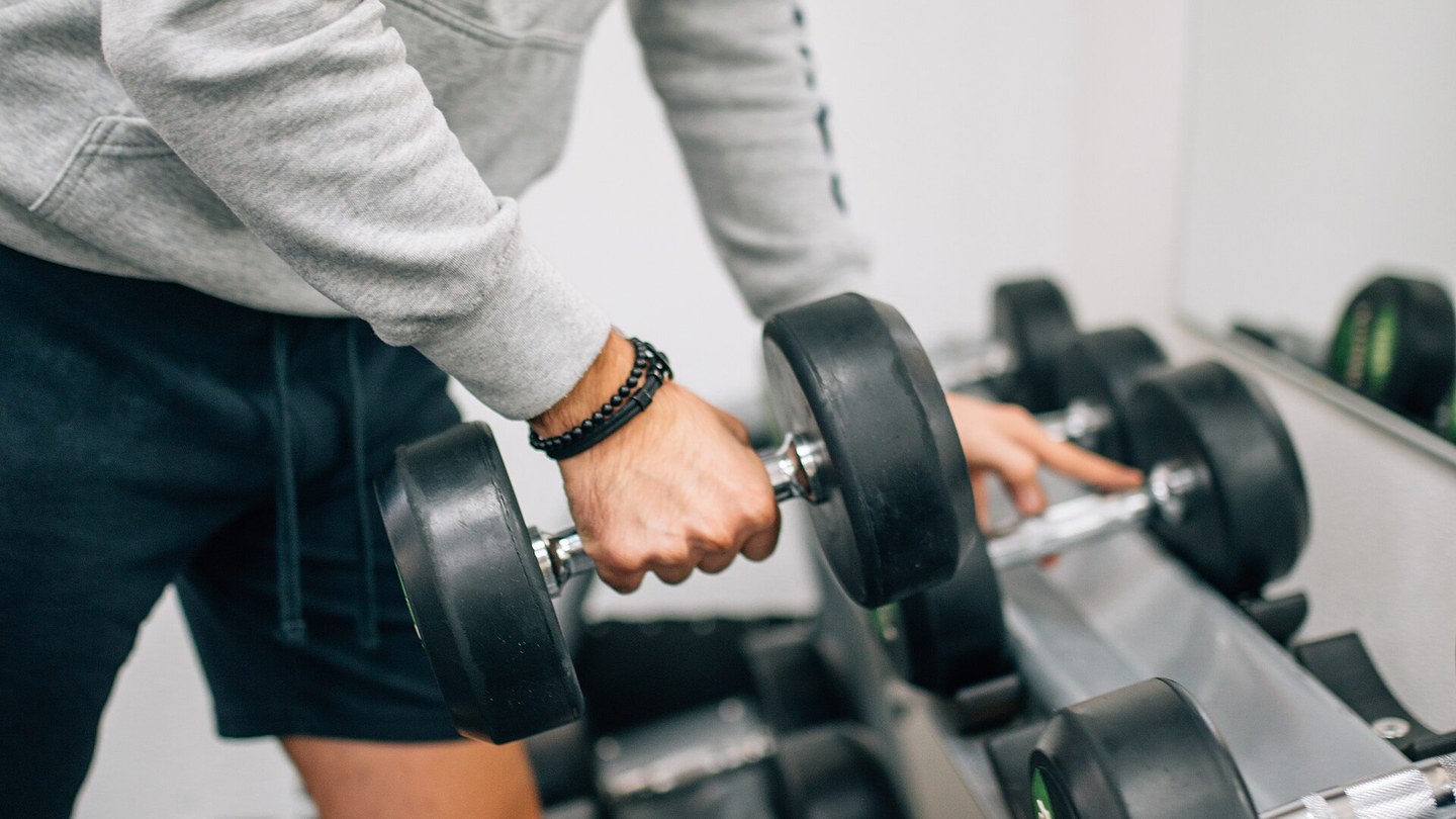 Sportive réalisant une fente statique avec haltères dans une salle de sport lumineuse